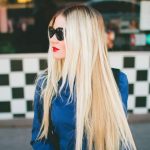 Barefoot Blonde Blogger shows off her long blonde hair extensions, paired with a blue coat, sunglasses, and slick of red lipstick.