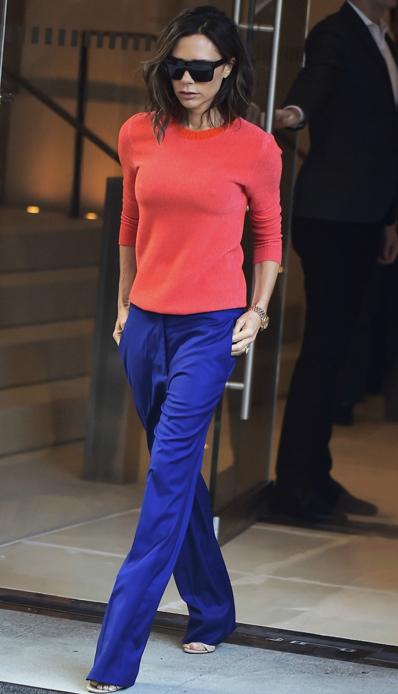 Victoria Beckham street style wearing orange cashmere jumper with blue trousers, sunglasses and heels