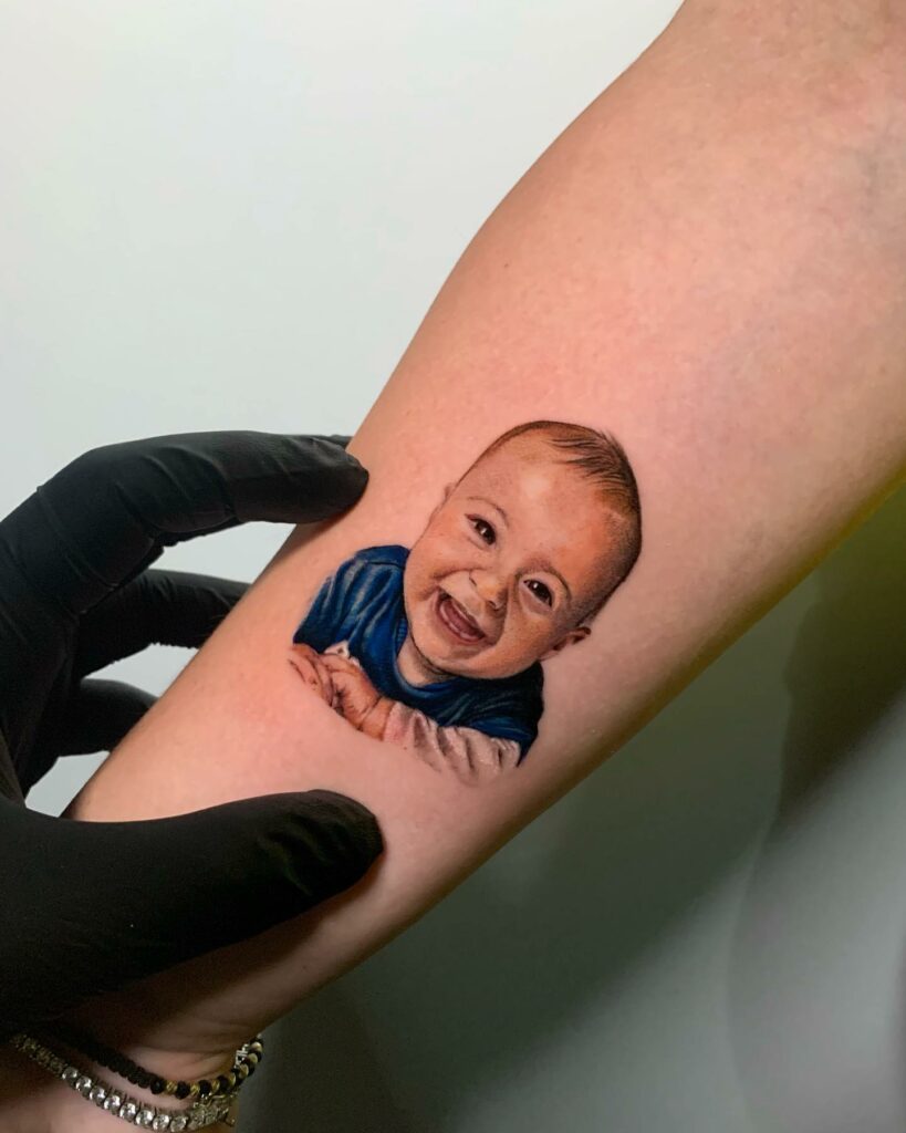 Download A Man Holding A Baby With Tattoos On His Chest | Wallpapers.com