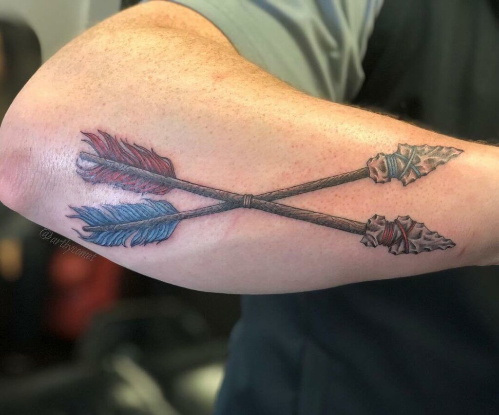 Small arrow tattoo on the left forearm.